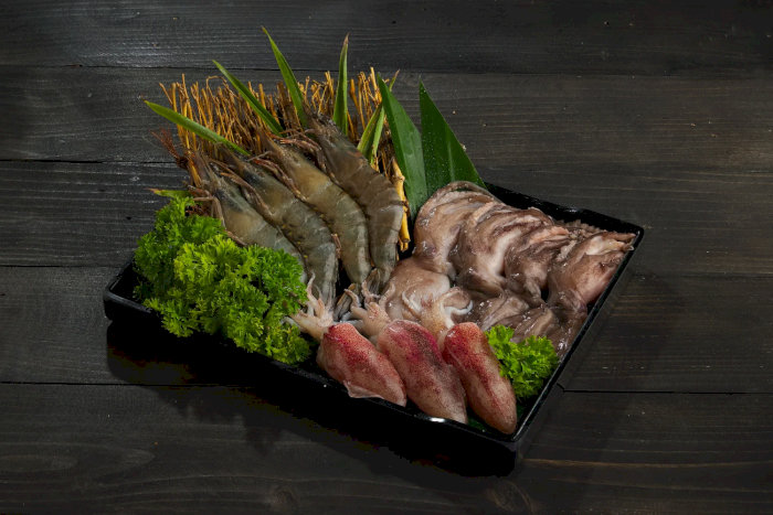 Khay hải sản tươi sống gồm tôm, mực trứng, bạch tuộc và rau trang trí trên nền gỗ đen sang trọng.