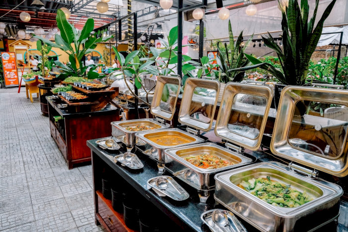Quầy buffet với nhiều món ăn nóng được giữ ấm trong các khay inox sáng bóng, bày trí hấp dẫn, sẵn sàng phục vụ thực khách.