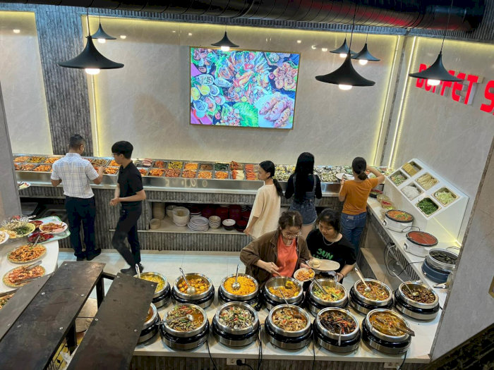 Thực khách chọn món tại quầy buffet tự chọn với đa dạng món ăn nóng, salad và rau tươi trong không gian hiện đại.