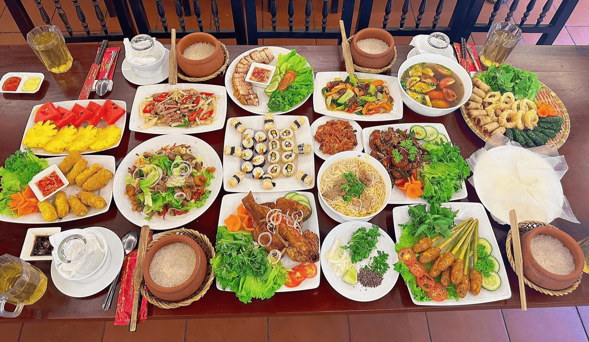 Bữa cơm đủ đầy, thịnh soạn tại Nhà hàng Cơm Sen Bàn ăn dài bày biện vô số món ăn hấp dẫn, từ cơm niêu, nem rán, gỏi cuốn, nộm, gà nướng, mì xào, sushi đến trái cây tươi, nước sâm mát lạnh.