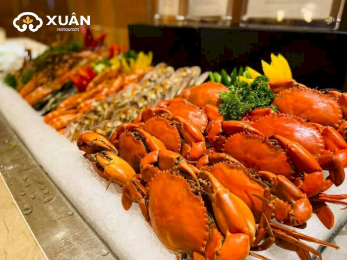 Quầy hải sản tươi ngon tại nhà hàng Xuân với ghẹ hấp đỏ au, tôm sú hấp, cá nướng và các loại hải sản khác được bày trên đá lạnh, trang trí bắt mắt.