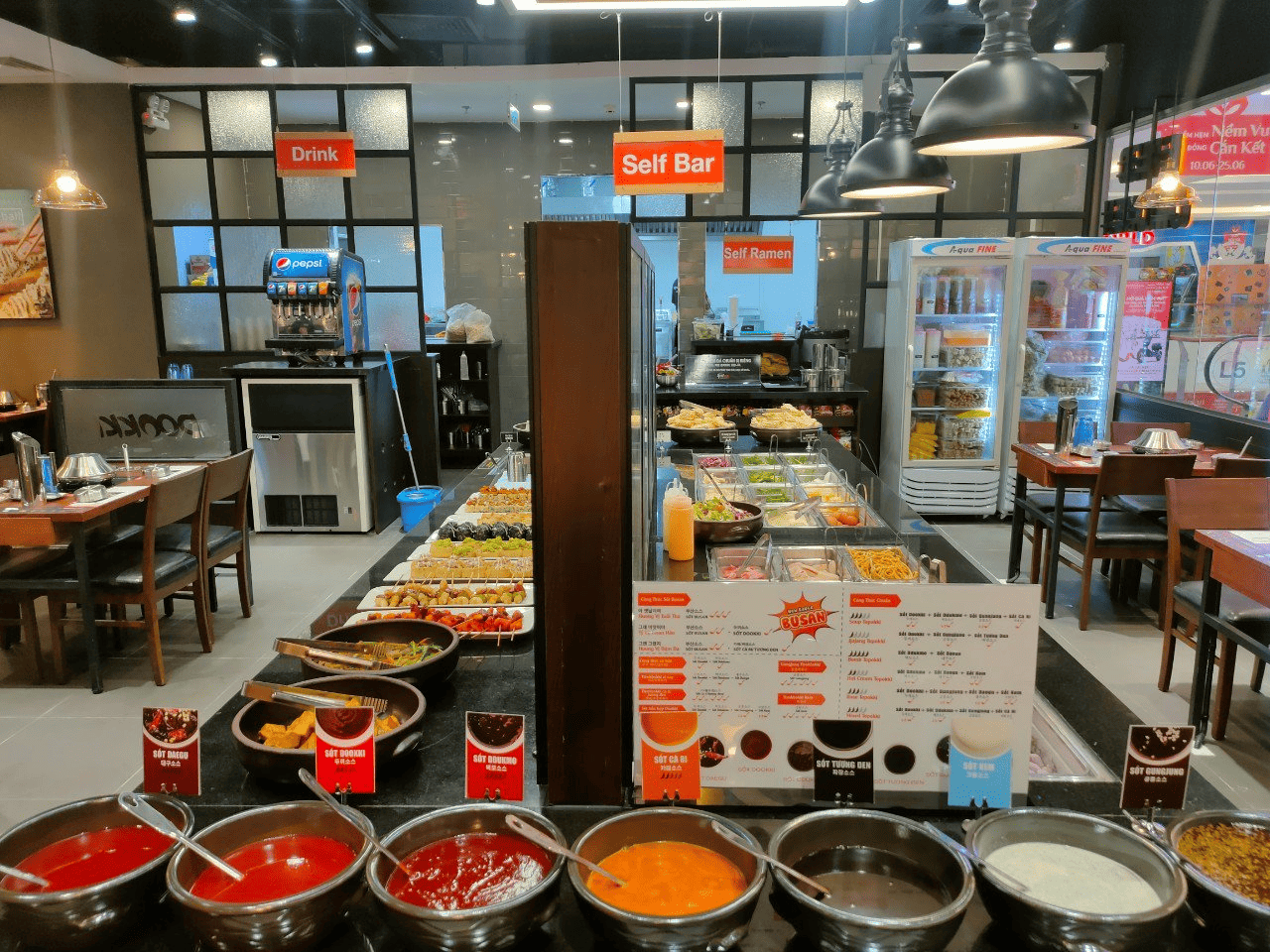 Góc nhìn rộng về khu vực buffet tự chọn tại nhà hàng Dookki với quầy topping đa dạng, các loại nước sốt hấp dẫn và khu vực đồ uống mát lạnh