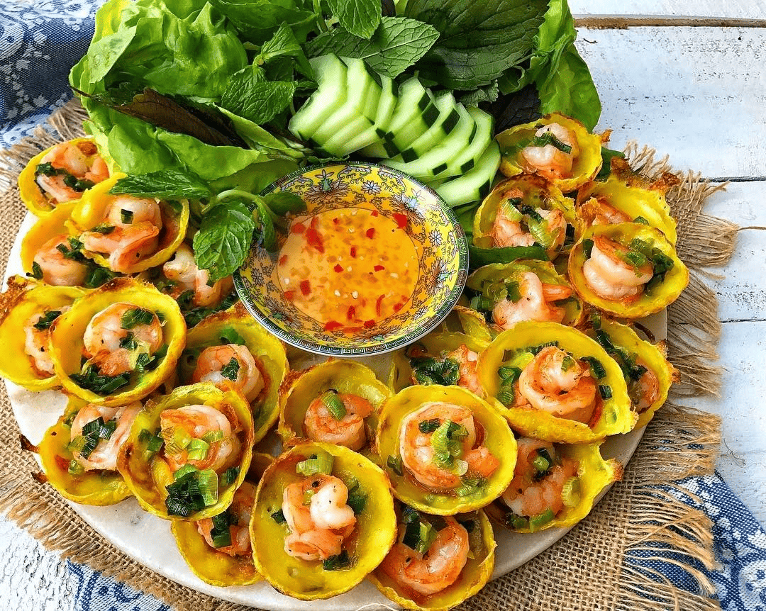 Đĩa bánh khọt vàng giòn, tôm thịt tươi ngon, rau sống xanh mát và chén nước mắm chua ngọt hấp dẫn