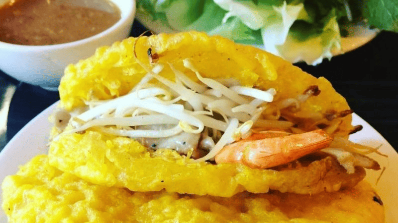 Chiếc bánh xèo vàng rộm, giòn tan, nhân tôm thịt đầy đặn, thêm chút giá đỗ tươi ngon, ăn kèm rau sống và nước chấm đậm đà