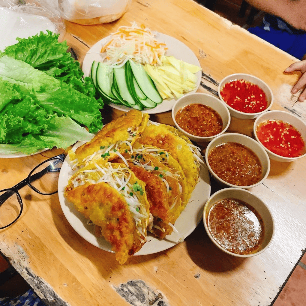 Đĩa bánh xèo vàng ươm, nhân tôm thịt hấp dẫn, ăn kèm rau sống tươi xanh, dưa góp và các loại nước chấm đậm đà