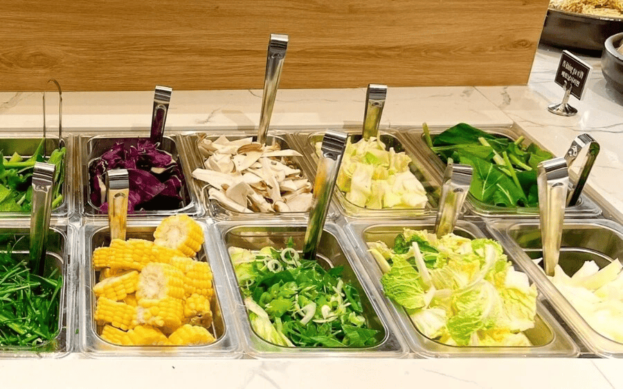 Quầy salad tự chọn phong phú với nhiều loại rau củ tươi ngon như bắp cải, rau bina, nấm, hành tây tím và ngô vàng hấp dẫn.