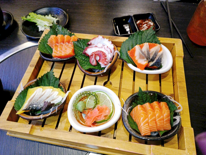 Set sashimi Nhật Bản gồm cá hồi, bạch tuộc, cá trích ép trứng, phục vụ trên mẹt tre kèm lá tía tô và chanh tươi.