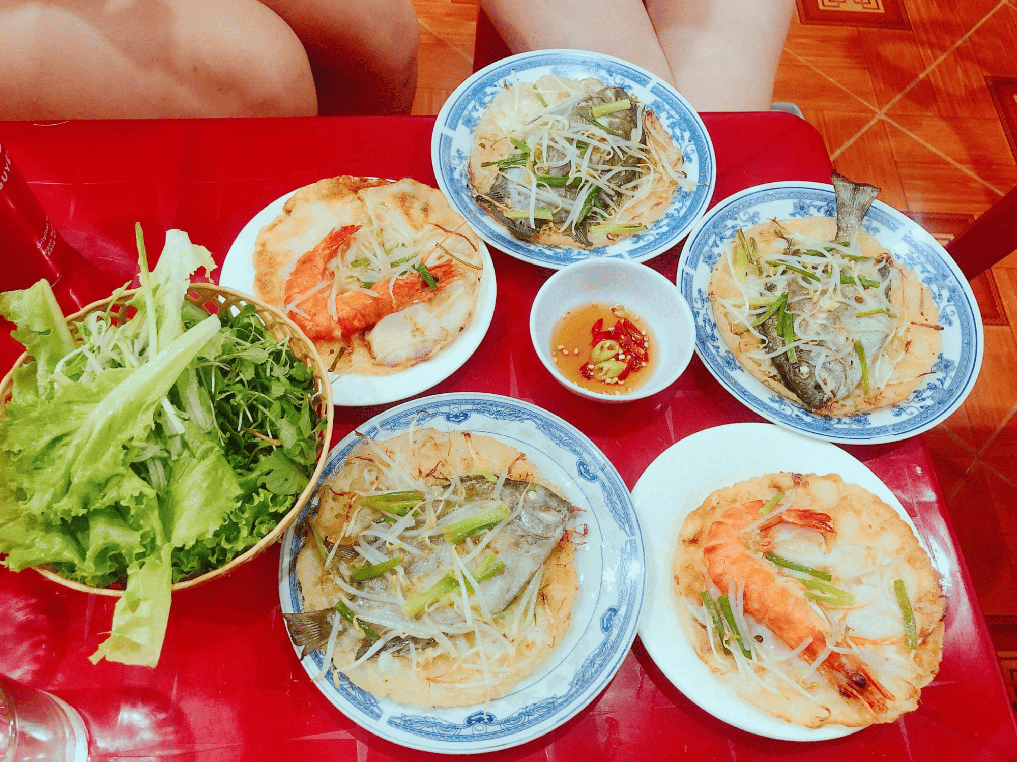 Bàn ăn với những chiếc bánh xèo giòn tan, bên trên có cá kình tươi ngon, tôm đỏ au, rau sống và chén nước chấm đậm đà