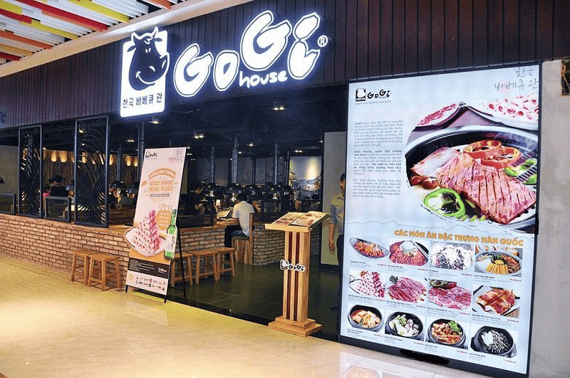 Mặt tiền nổi bật của nhà hàng thịt nướng Hàn Quốc GoGi House với biển hiệu lớn phát sáng và menu các món nướng hấp dẫn được trưng bày ngay bên ngoài.