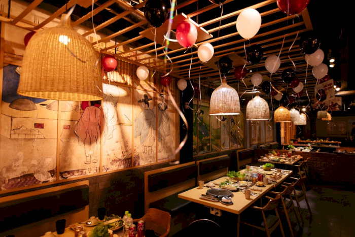  Nội thất nhà hàng GoGi House với bàn ghế gỗ, đèn lồng trang trí và bóng bay nhiều màu sắc tạo không khí ấm áp, thân thiện.