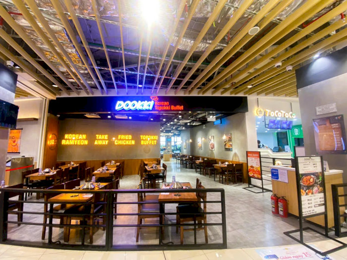 Không gian hiện đại của nhà hàng buffet lẩu tokbokki Dookki với nhiều bàn ăn gỗ và quầy line tự chọn ở phía trong.