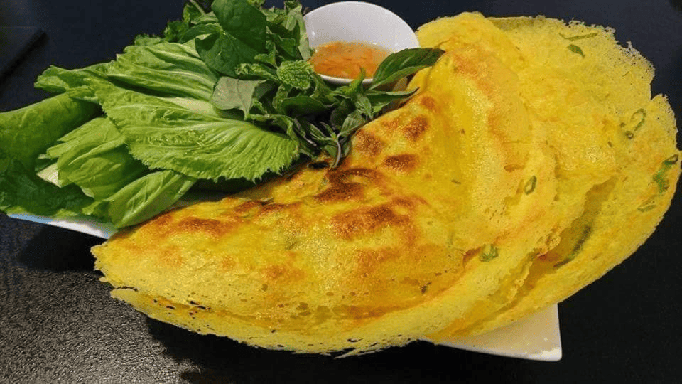 Đĩa bánh xèo màu vàng tươi, giòn rụm, ăn kèm rau sống xanh mát và chén nước chấm chua ngọt hấp dẫn