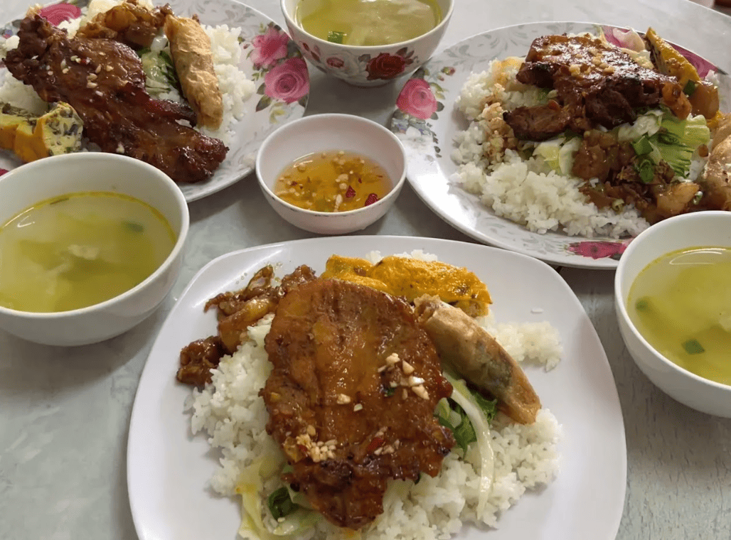 Cơm tấm sườn nướng là món ăn được yêu thích nhất tại quán cơm dì Mến Ba đĩa cơm tấm trắng dẻo với sườn nướng thơm lừng, bì heo thái sợi, chả trứng hấp dẫn, ăn kèm dưa chuột, cà chua, chén nước mắm chua ngọt và ba bát canh trong veo