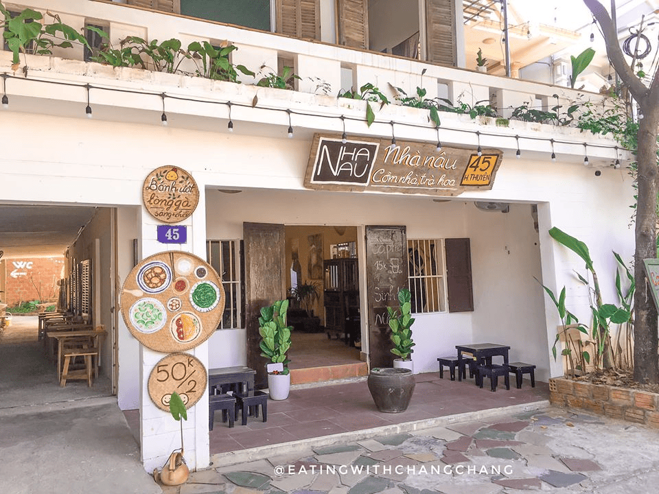 Mặt tiền qu&aacute;n Nh&agrave; N&acirc;u - Cơm nh&agrave; & Tr&agrave; Hoa tại địa chỉ 45 [c&oacute; thể l&agrave; t&ecirc;n đường hoặc khu vực ở Thừa Thi&ecirc;n Huế], với biển hiệu gỗ mộc mạc, trang tr&iacute; c&acirc;y xanh.