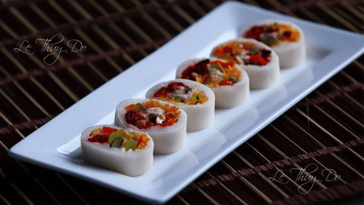  Năm khoanh bánh bó mứt hình trụ, lớp vỏ bánh trắng mịn bao bọc phần nhân mứt nhiều màu sắc hấp dẫn được bày trên đĩa chữ nhật