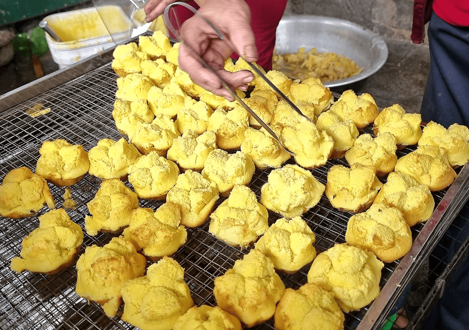 Mẻ bánh thuẫn mới ra lò có màu vàng tươi hấp dẫn, xốp mềm, được gắp bằng kẹp đặt trên vỉ nướng để nguội