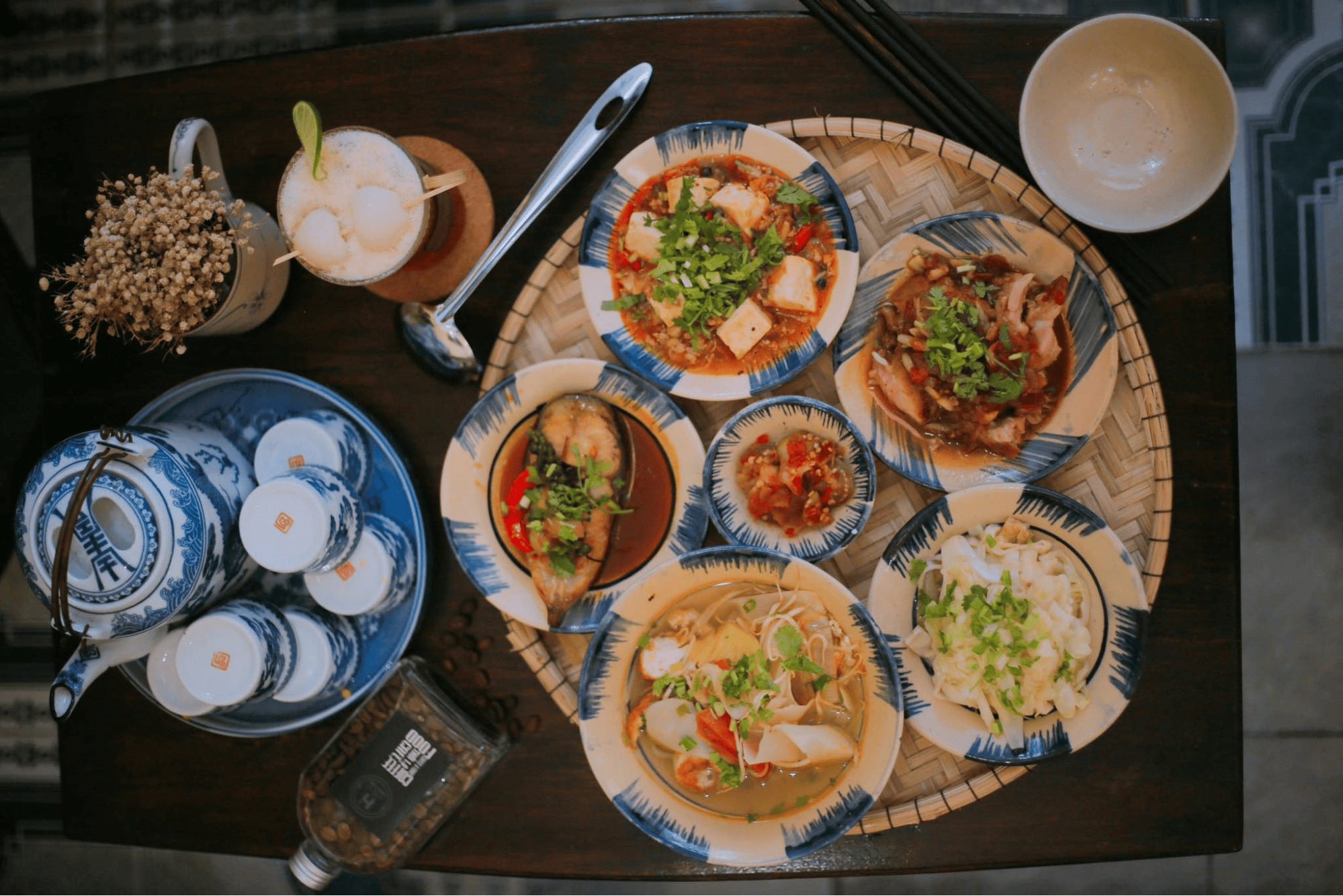 Thưởng thức mẹt cơm siêu ngon, đậm hương vị gia đình tại Cơm mẹt gia đình thời Z 1.0 Mẹt tre tròn bày biện các món ăn đặc trưng của ẩm thực Huế, bao gồm bát cơm trắng, cá kho riêu, thịt heo quay, canh rau, nộm và một chén mắm ớt nhỏ
