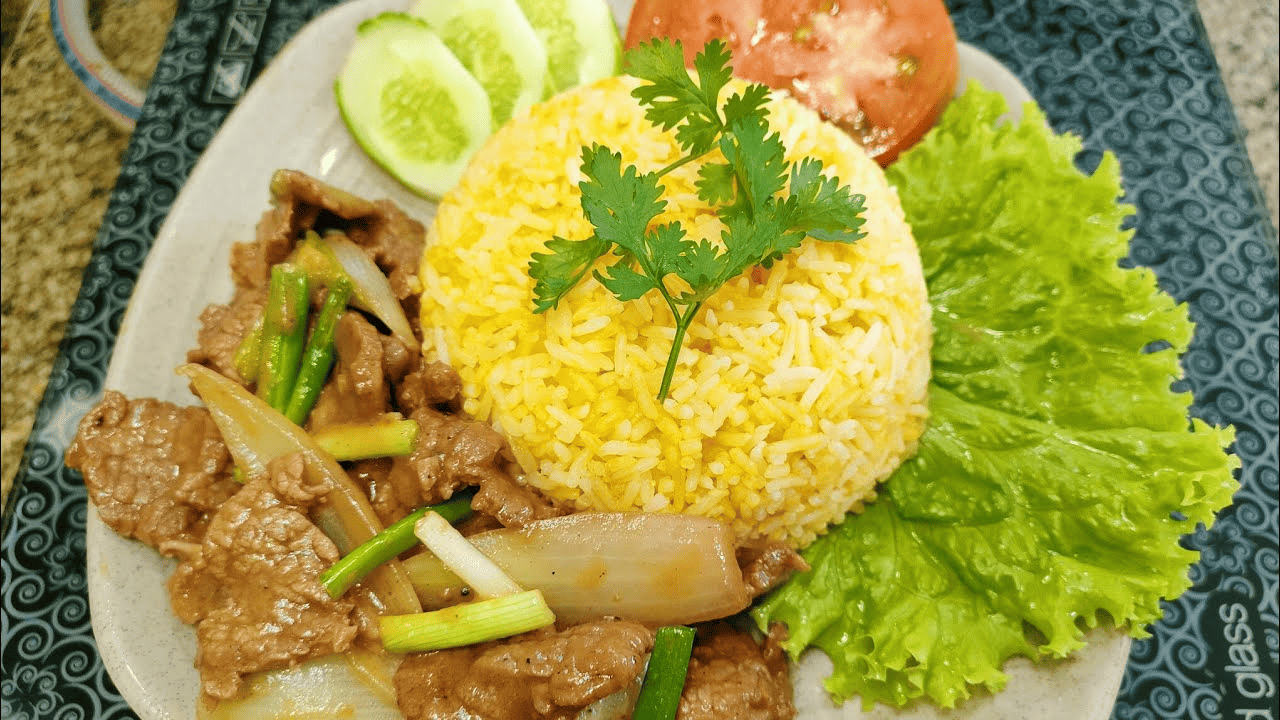 Cơm gà A Thiện với phần cơm thơm ngon, bắt mắt Đĩa cơm chiên vàng óng, tơi xốp, ăn kèm thịt bò xào mềm thơm, hành lá xanh tươi, vài lát dưa chuột, cà chua và rau xà lách tươi mát