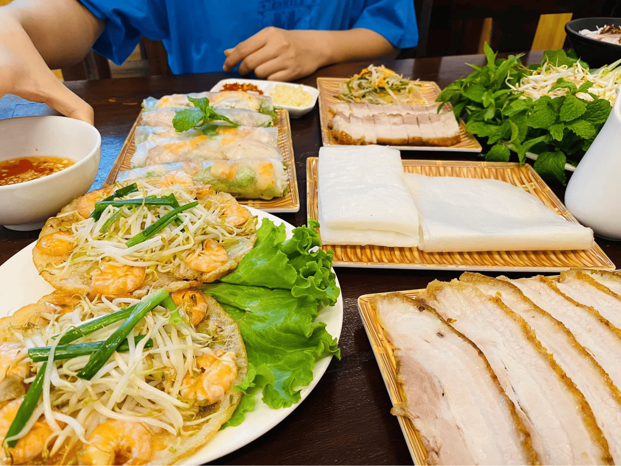 Bàn ăn với bánh xèo tôm giòn rụm, gỏi cuốn tươi ngon, thịt heo luộc, rau sống và chén nước chấm đậm đà, bữa ăn hấp dẫn
