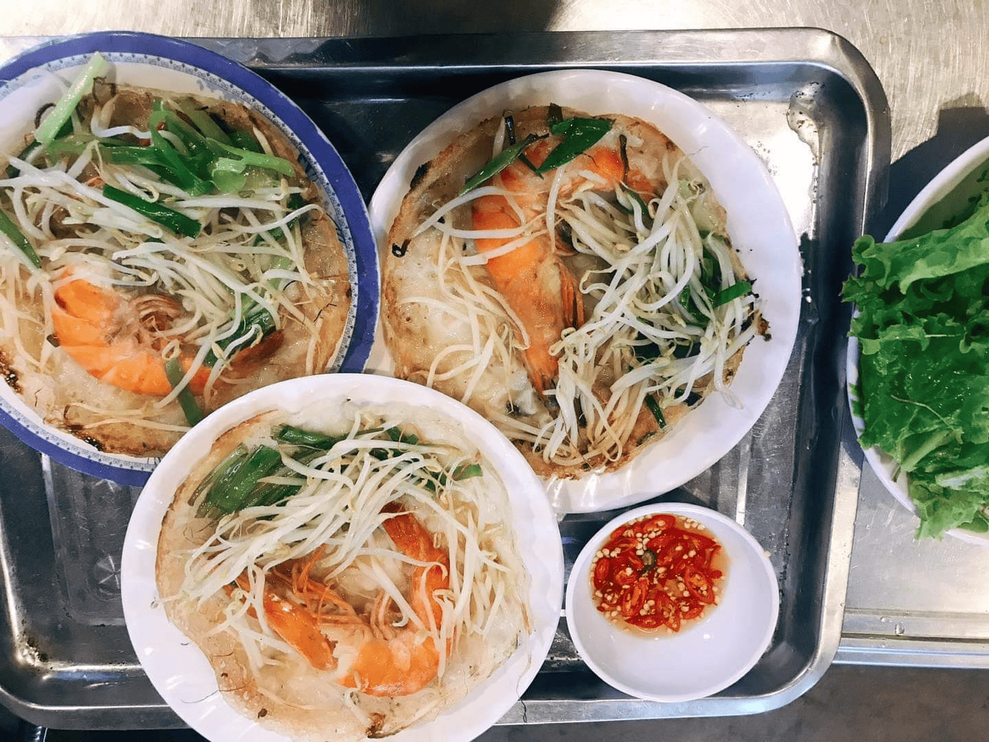  Ba chiếc bánh xèo vàng giòn với tôm tươi, giá đỗ và hành lá, ăn kèm rau sống và chén nước mắm ớt hấp dẫn