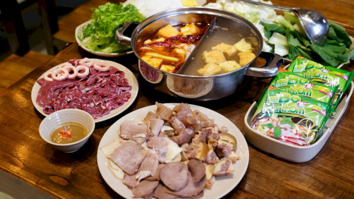 Bàn ăn lẩu bò nhúng dấm tại Hà Nội với nồi lẩu hai ngăn, thịt bò tươi, rau xanh và bún.