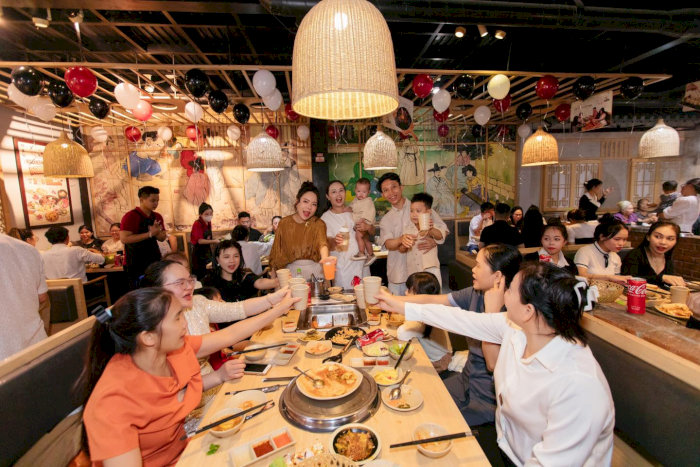 nhà hàng lẩu nướng với nhiều khách hàng đang tụ tập ăn uống, nâng ly trang trí ấm cúng với đèn lồng và bóng bay.