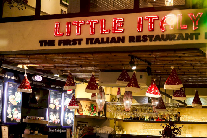 Mặt tiền nhà hàng Ý Little Italy với biển hiệu đèn neon nổi bật và trang trí mũ ông già Noel độc đáo.
