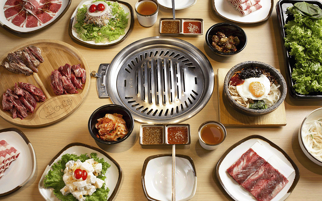 Bàn ăn đầy ắp các món nướng hấp dẫn tại GoGi House, bao gồm thịt bò tươi ngon, sườn heo tẩm ướp đậm đà, panchan đa dạng và bếp nướng than hoa ở trung tâm 